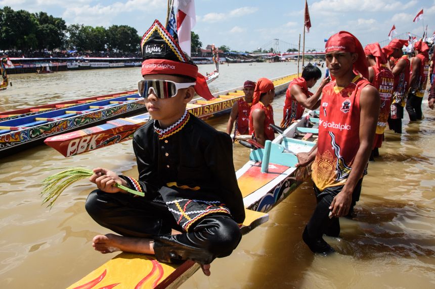 Rayyan Arkan Dikha (L), an 11-year-old boy who went viral for his calm dance on the bow of a traditional longboat, sits on his team's vessel before competition during the Pacu Jalur longboat race festival on the Kuantan River in Kuantan Singingi Regency, Riau Province, on August 22, 2025. Armed with colourful oars, rowers pack into long boats in western Indonesia, paddling furiously in front of race crowds swelled by the viral success of a young boy famous for his dancing at the front of the traditional vessels.