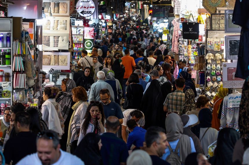 People walk past shops and browse for goods at the Grand Bazaar in Tehran on August 24, 2026. Oil prices fell on August 24 as investors braced for details of a US plan to isolate the Iranian economy that President Donald Trump billed as the
