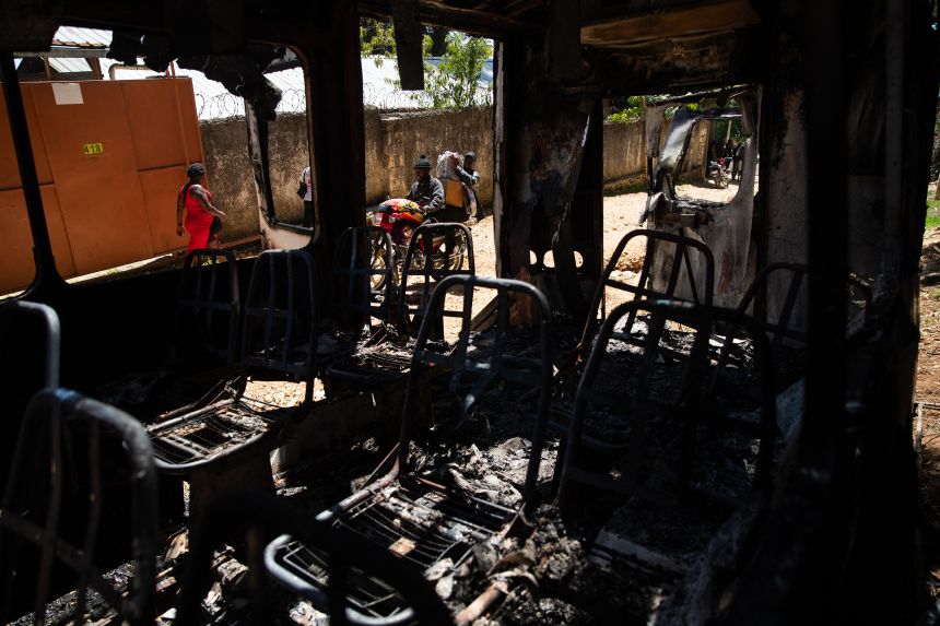 People walk past the remains of a charred vehicle following overnight violence where more than twenty people were killed by armed gangs in Kenscoff, a neighborhood near Port-au-Prince, Haiti, on August 24.